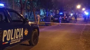 Fotografía nocturna de un operativo policial en una calle de Rosario. Se observan patrulleros con las balizas encendidas y, en primer plano, una cinta de peligro de color blanca y roja que delimita el perímetro de seguridad en la zona donde se produjeron los disparos.