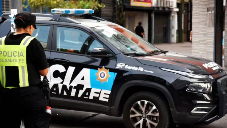 Fotografía de archivo de un patrullero de la Policía de la Provincia de Santa Fe estacionado en la calle, con las luces de emergencia apagadas. El plano es medio y enfoca el lateral del vehículo donde se lee la inscripción de la fuerza de seguridad sobre un fondo oscuro con tonos azules y negros.